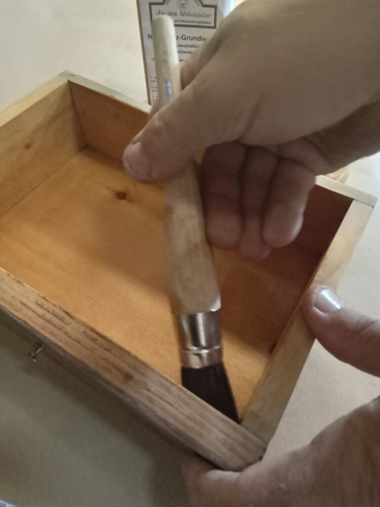 Fachgerechtes Ausstreichen einer unlackierten Holzschublade mit der Naturharz-Grundierung zur Beseitigung von muffigen Gerüchen.
